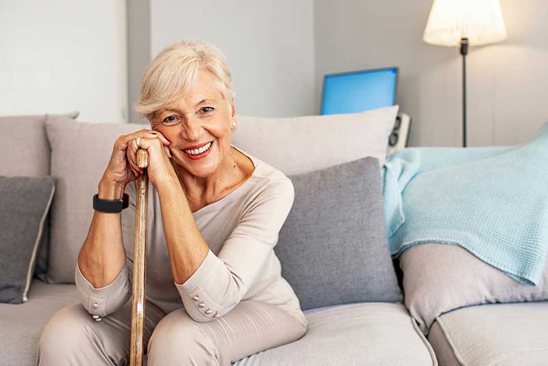 older woman leaning on cane with a smile